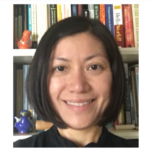 Headshot of Dr. Edna Tan, wearing a black shirt and sanding in front of a bookshelf with books and two small ceramic birds (one blue and one orange)