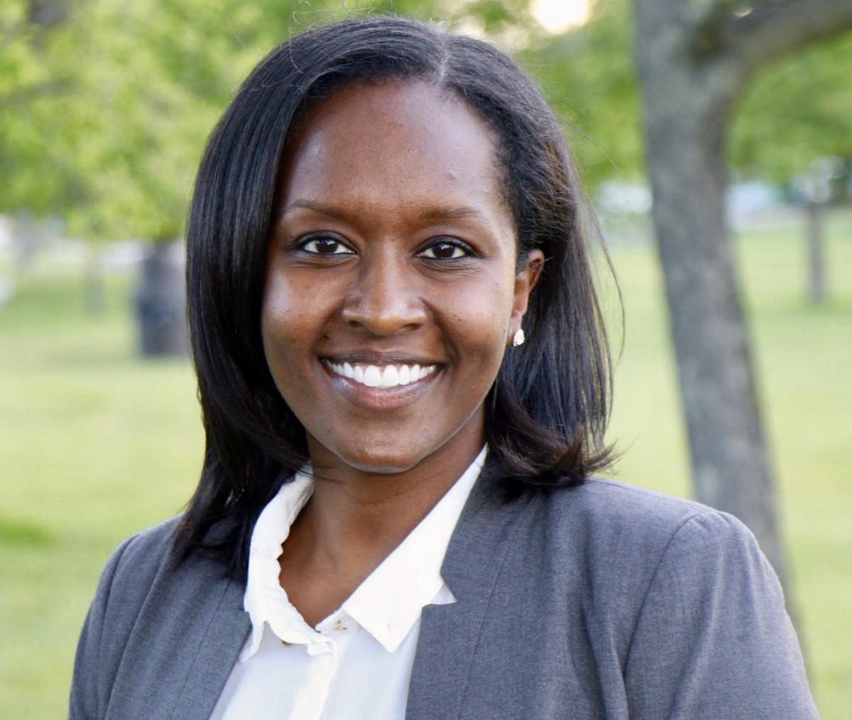 Dr. Meseret Hailu in a white collared shirt and grey blazer outside in grass with trees