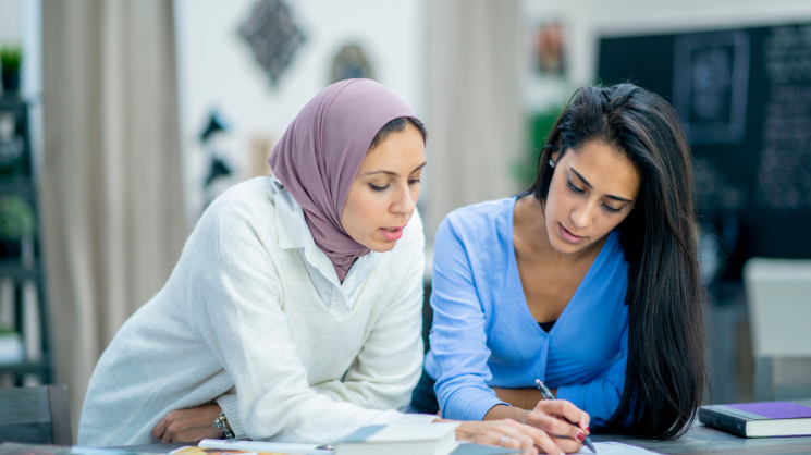 two muslim women (one with hijab, one without) studying