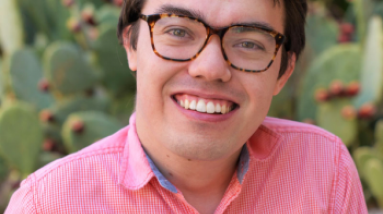 Headshot of Logan Gin in a red and white checkered shirt and brown glasses in front of a prickly pear cactus