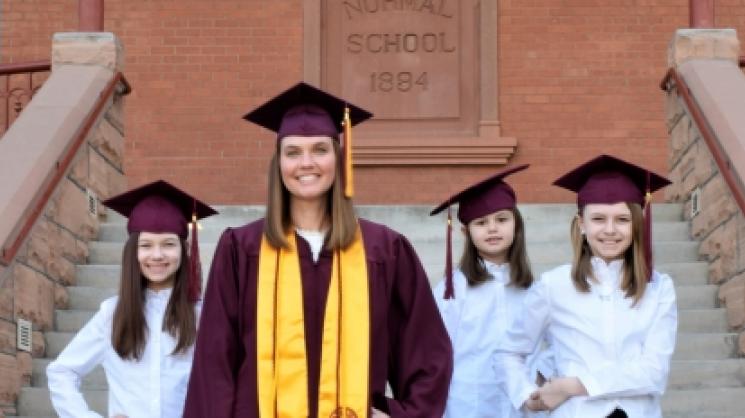 julie roberts in graduation uniform with three daughters in all white outfits in front of an ASU backdrop.